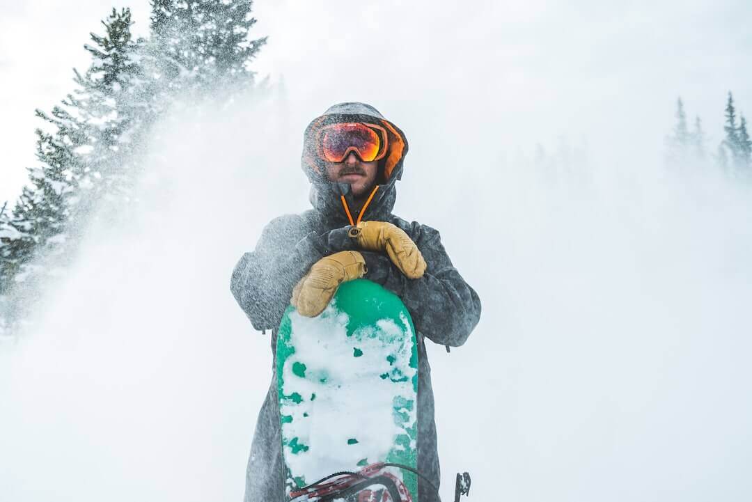 Snowboarder in winter gear surrounded by snow and trees, showcasing extreme sports style and adventure.