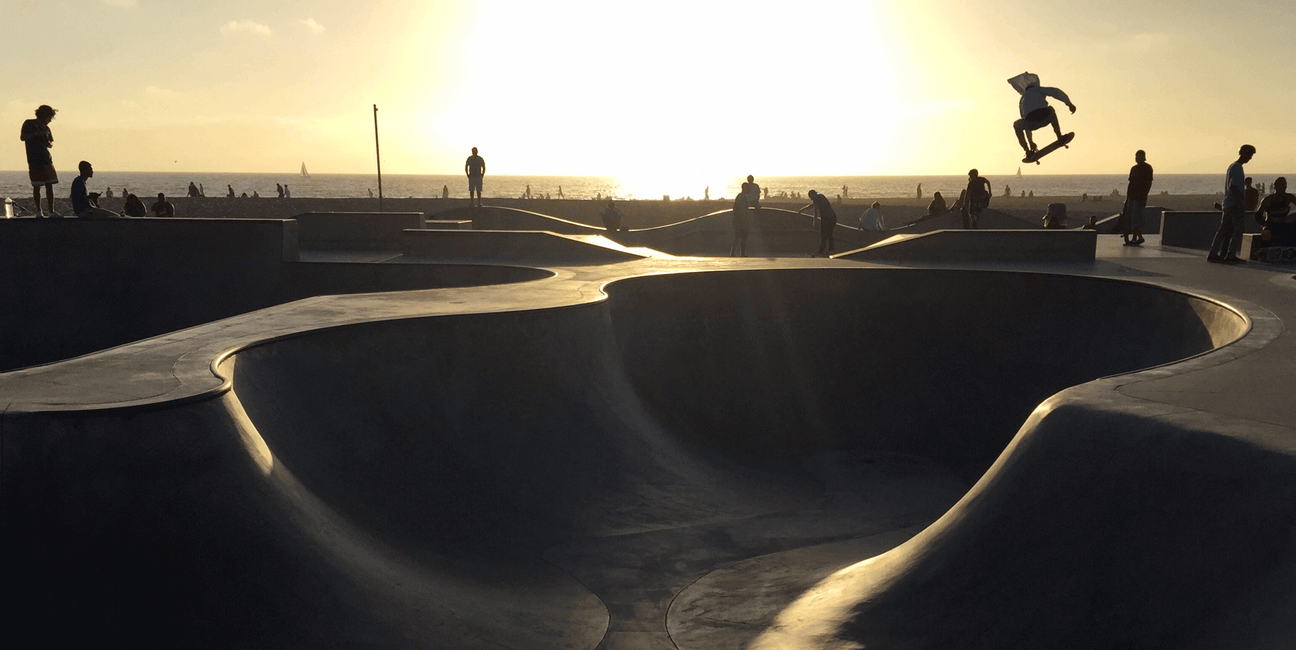 Skateboarder performing tricks at sunset in a skatepark.