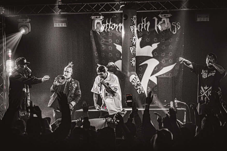 Kottonmouth Kings performing on stage during their 2024 comeback tour in a black and white shot with an energetic crowd.