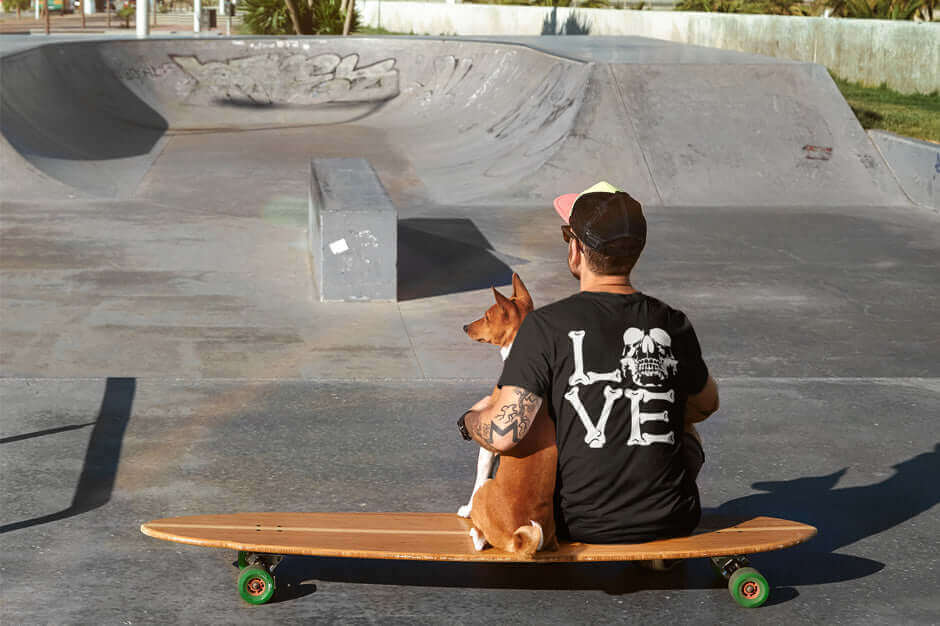 Man with dog on skateboard at urban skatepark, wearing Ghetto Rags shirt, embracing edgy street style.