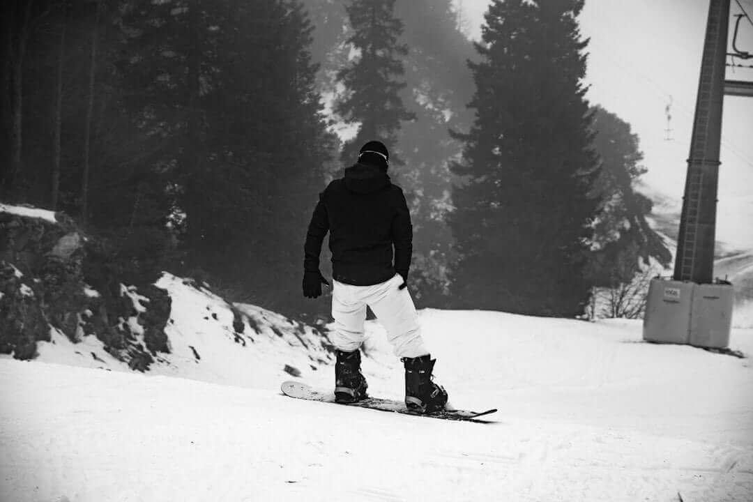 Snowboarder in winter attire gliding down a snowy slope surrounded by misty pine trees.