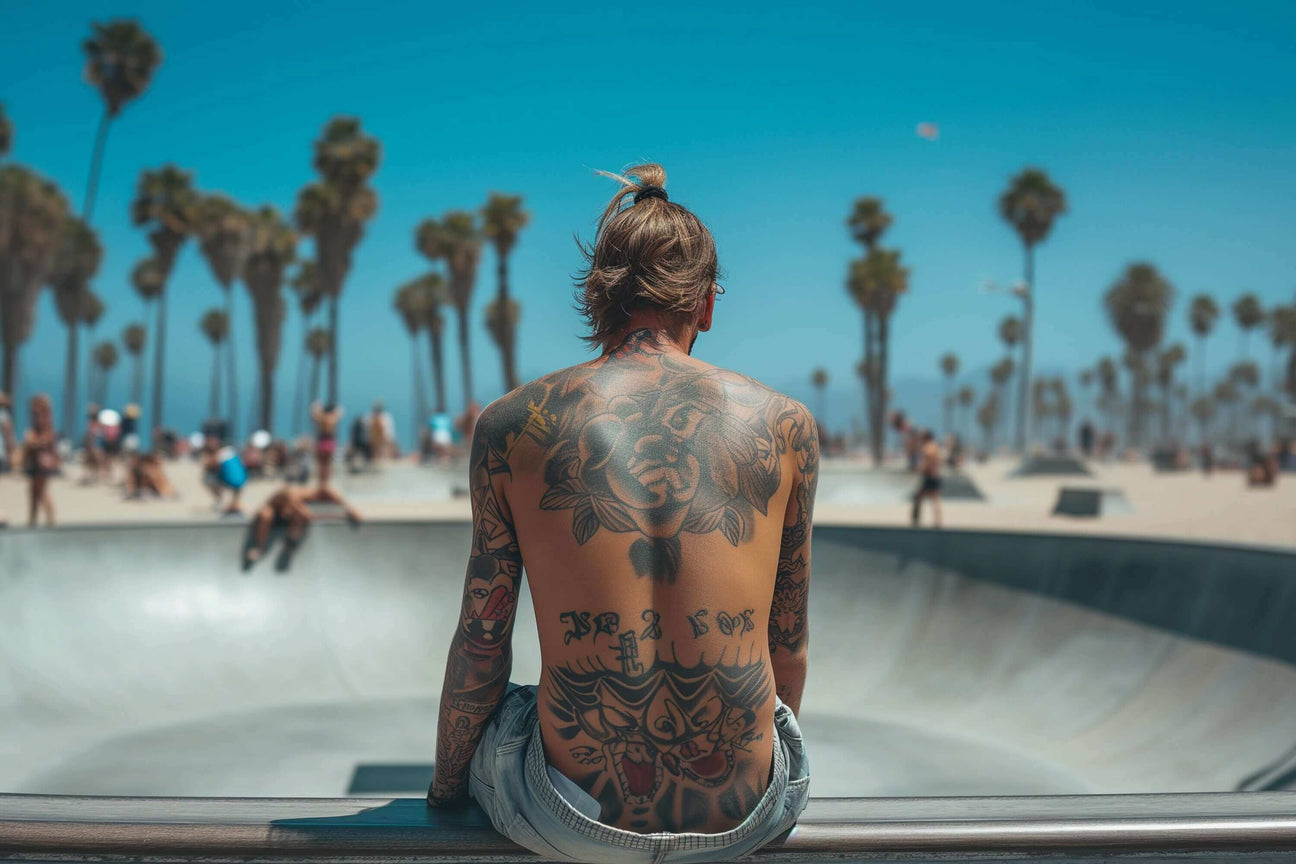 Skater with tattoos sitting at Venice Beach skate park on a sunny day.