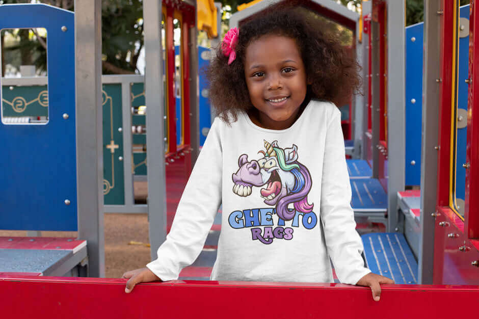 Smiling child wearing a Ghetto Rags Unicorns Unleashed long sleeve t-shirt on a colorful playground