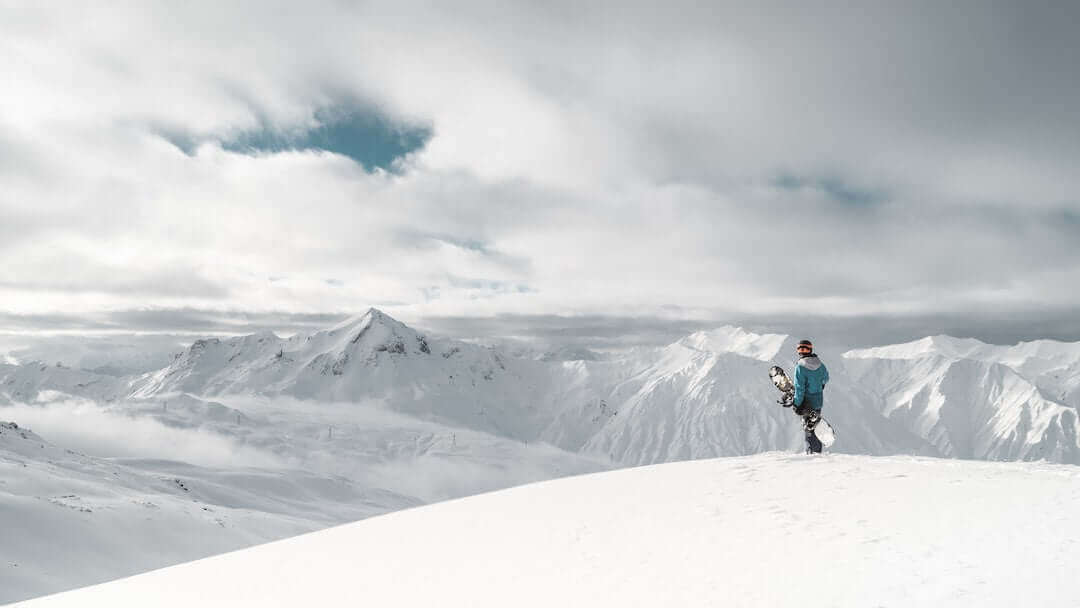 Snowboarder on a snowy mountain peak under cloudy sky, embracing winter adventure and scenic views.