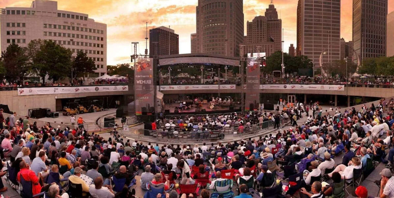 Large crowd at an outdoor live music concert in downtown Detroit during sunset.