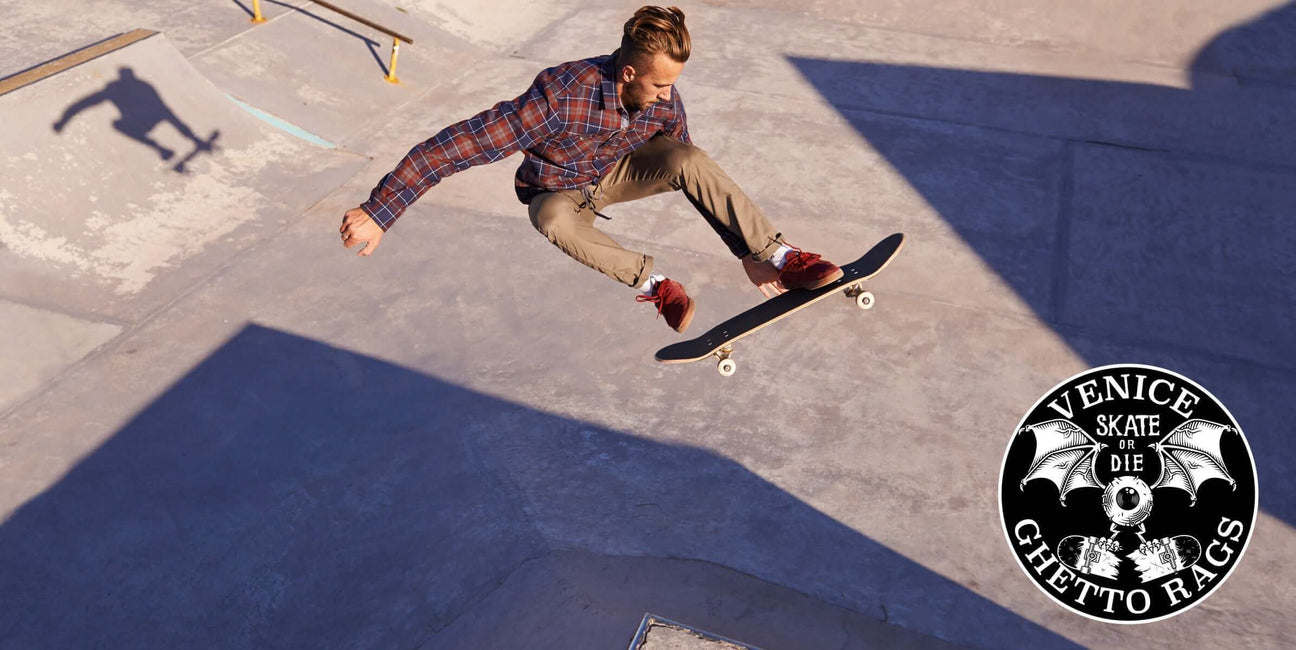 Skater performing aerial trick in urban skatepark wearing Ghetto Rags anti-workwear with Venice Skate or Die logo.