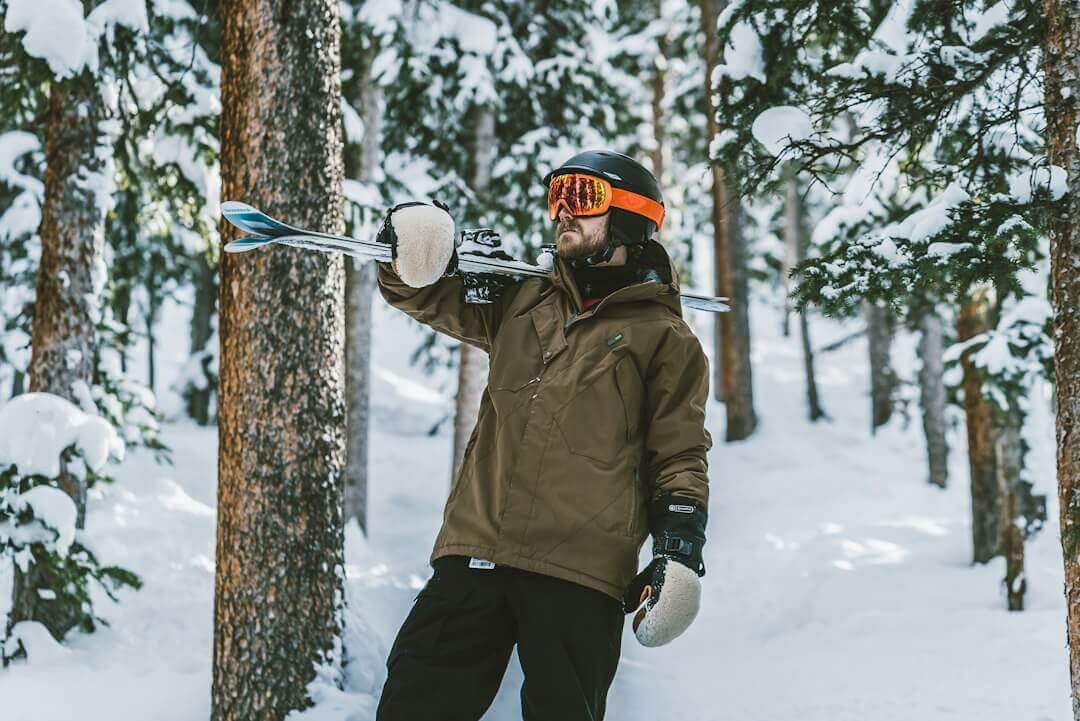 Man with skis and helmet in snowy forest showcasing rugged outerwear style.