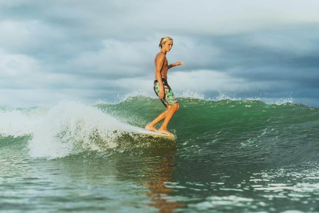 Surfer riding a wave under cloudy skies in stylish streetwear shorts