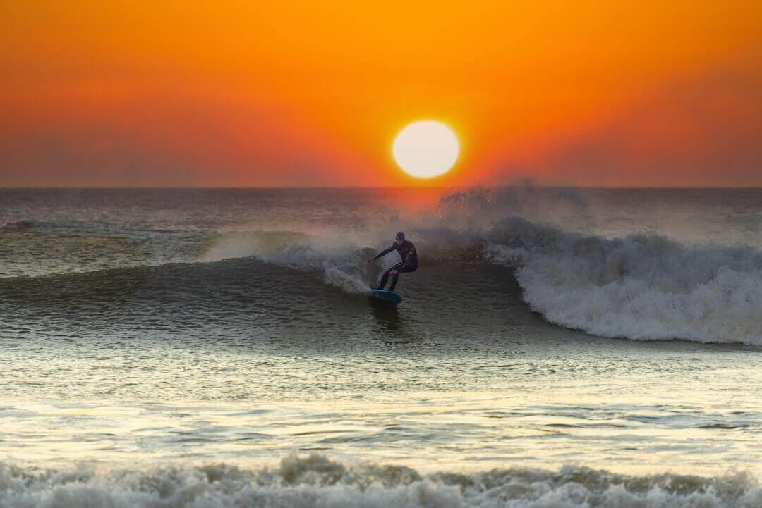 Surfer riding a wave at sunset, capturing surf-inspired style and energy for Ghetto Rags' streetwear collection.