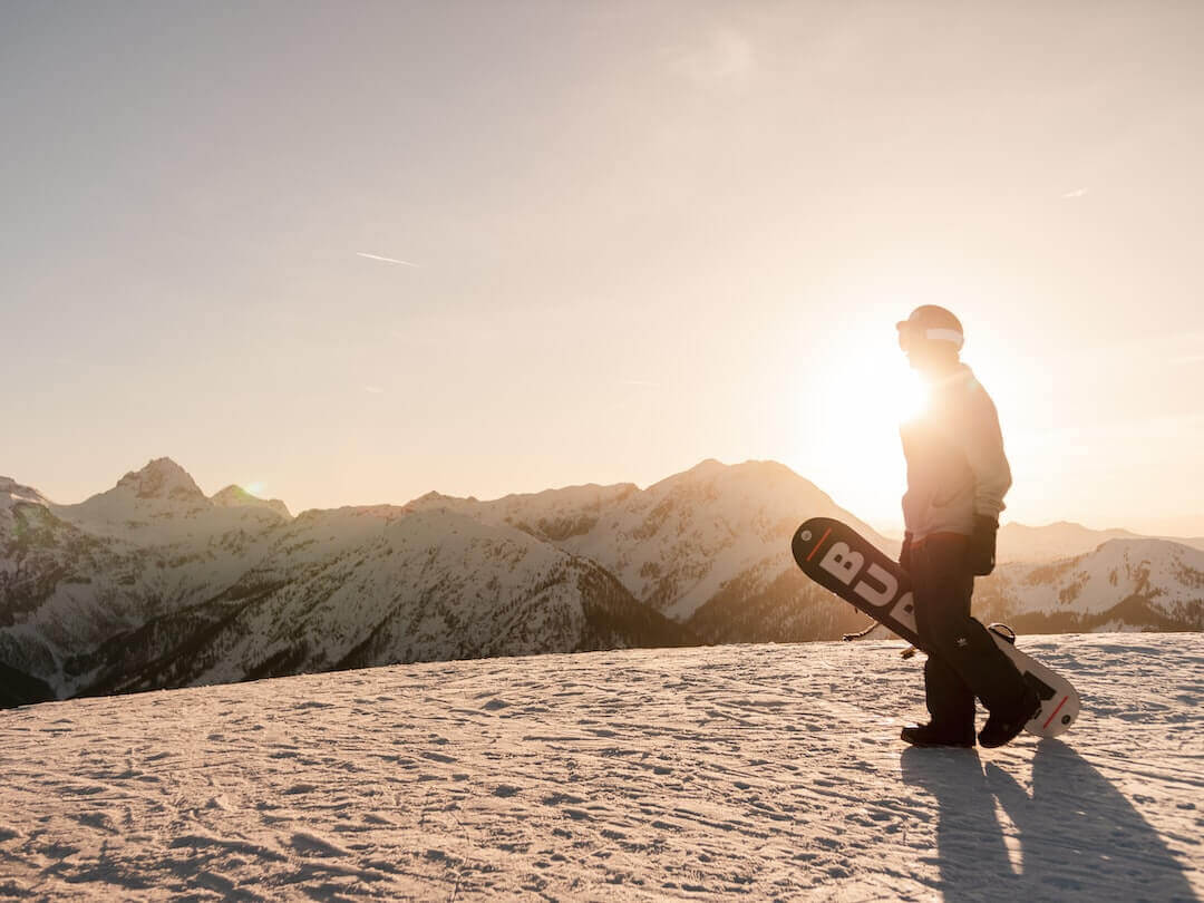 Snowboarder walking on a snowy mountain at sunset, highlighting the adventurous spirit of streetwear fashion.