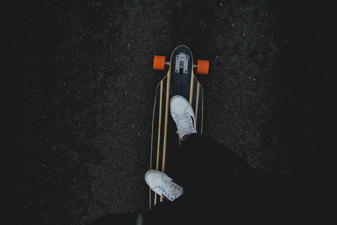 Skateboarder in white sneakers gliding on a stylish longboard, illustrating urban streetwear fashion trends.